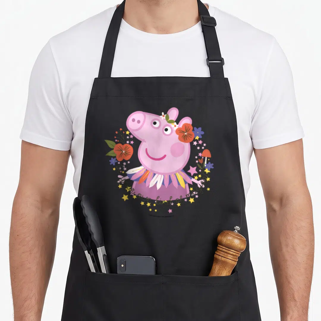 Magical crazy pig lady apron - Pink pig in flower wreath with stars and be your own kind of magical text — shown on a black cotton canvas apron against a white background