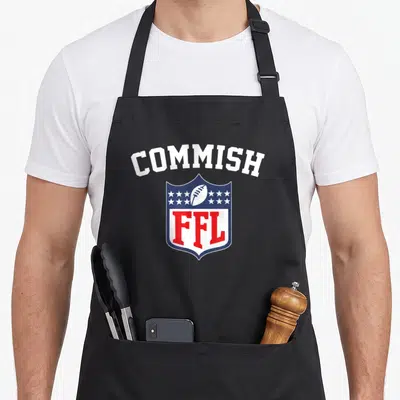 Commish football apron - White COMMISH text over blue red shield containing football and FFL letters — shown on a black cotton canvas apron against a white background
