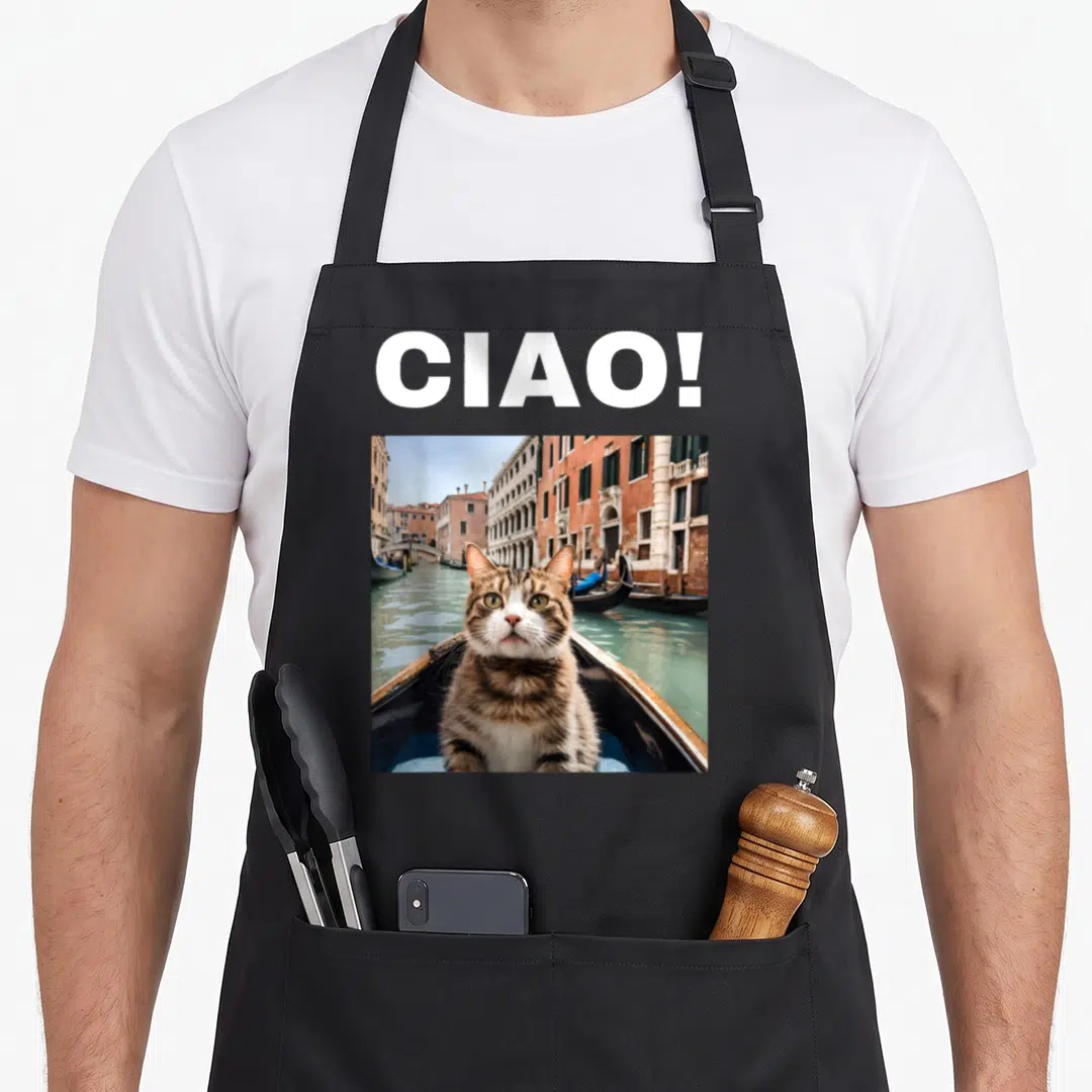 Ciao cat apron - White CIAO text above a square photo of a brown tabby cat sitting in a gondola on turquoise water — shown on a black cotton canvas apron against a white background