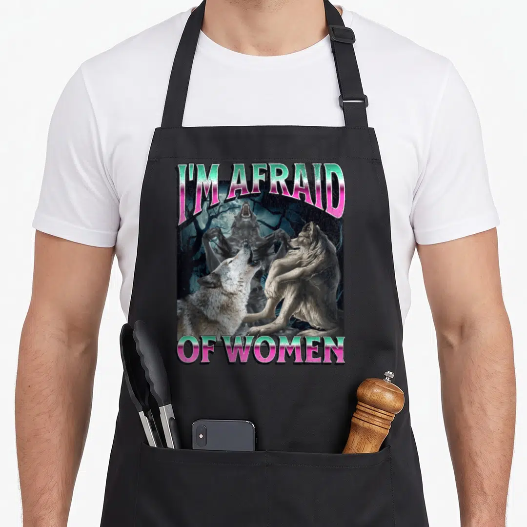 Afraid meme apron - I'M AFRAID OF WOMEN text with werewolves and moon in pink green grey black — shown on a black cotton canvas apron against a white background