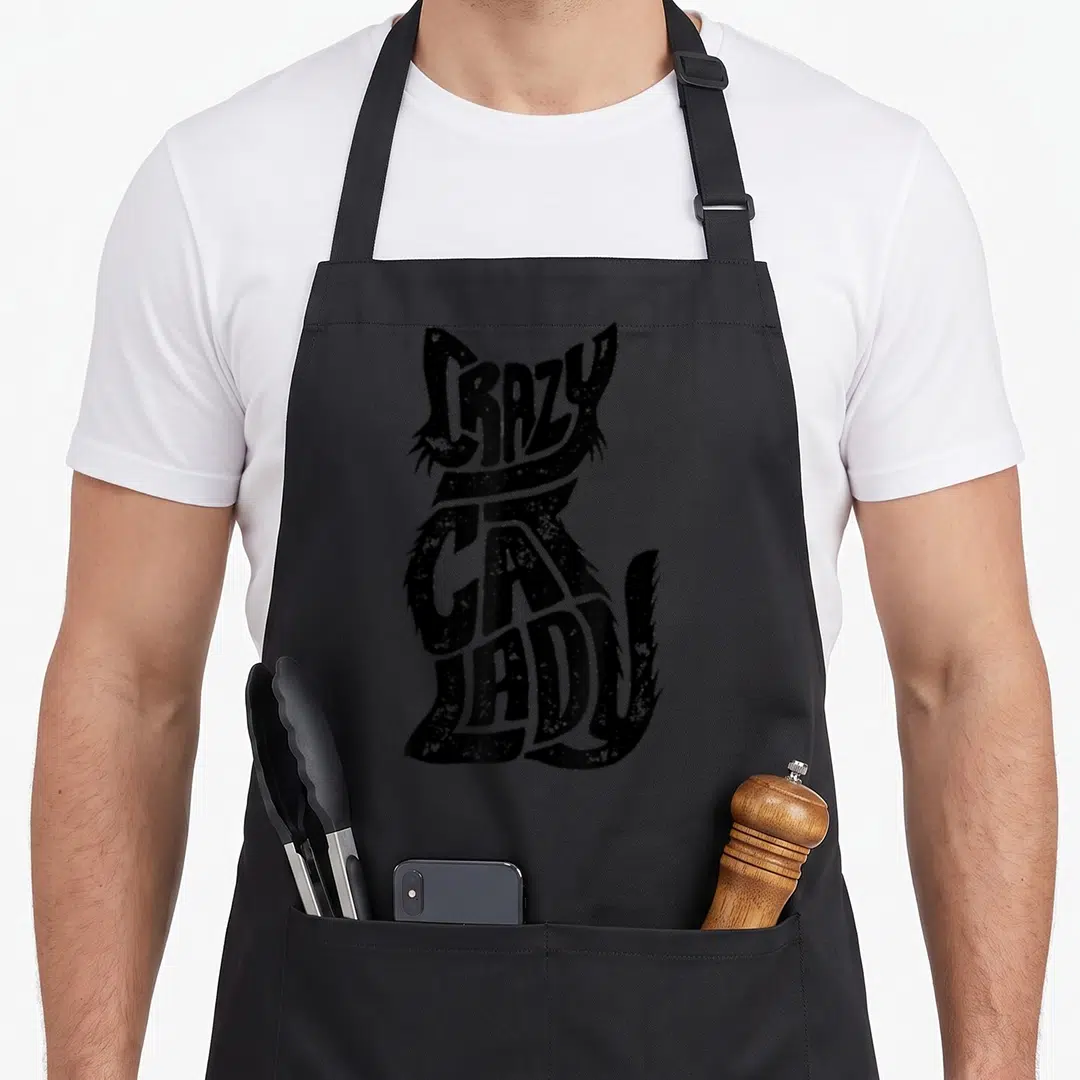 Kitty kitten crazy cat lady apron - Black distressed text spelling CRAZY CAT LADY arranged in the shape of a sitting — shown on a black cotton canvas apron against a white background