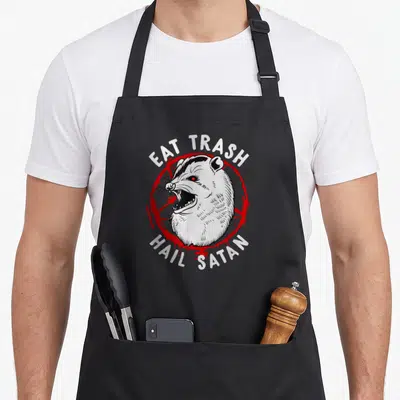 Eat i love watching apron - Cartoon opossum head over red pentagram with white text EAT TRASH HAIL SATAN — shown on a black cotton canvas apron against a white background