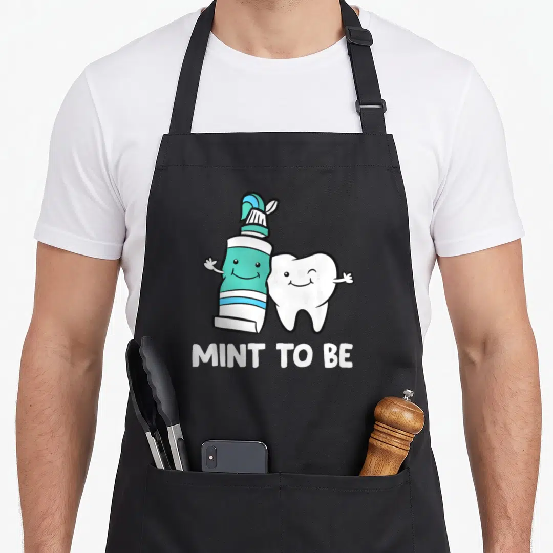 Mint dentist apron - Cartoon teal toothpaste and white tooth with mint to be text — shown on a black cotton canvas apron against a white background