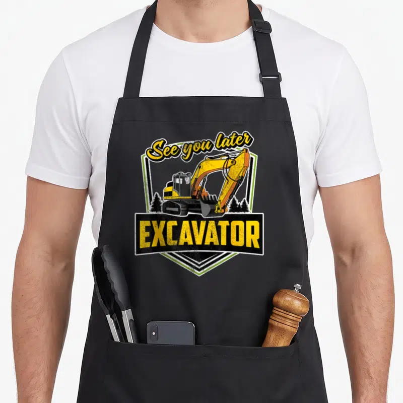 See heavy apron - Retro shield with yellow excavator and See you later EXCAVATOR text — shown on a black cotton canvas apron against a white background