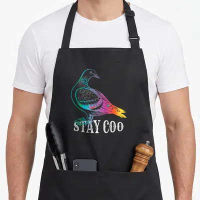 Pigeon bird apron - Rainbow cartoon pigeon illustration above white Stay Coo text — shown on a black cotton canvas apron against a white background