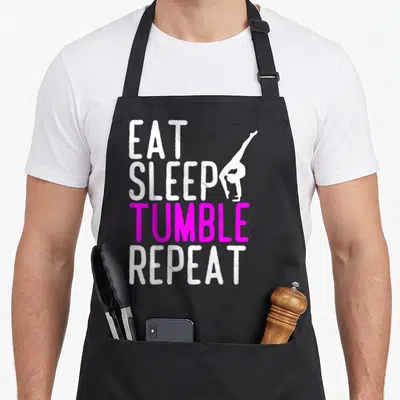 Eat gymnastics quotes apron - Stacked EAT SLEEP TUMBLE REPEAT text with white gymnast handstand silhouette — shown on a black cotton canvas apron against a white background
