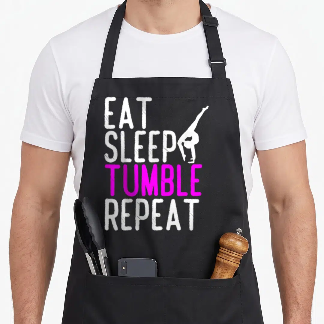 Eat gymnastics quotes apron - Stacked EAT SLEEP TUMBLE REPEAT text with white gymnast handstand silhouette — shown on a black cotton canvas apron against a white background