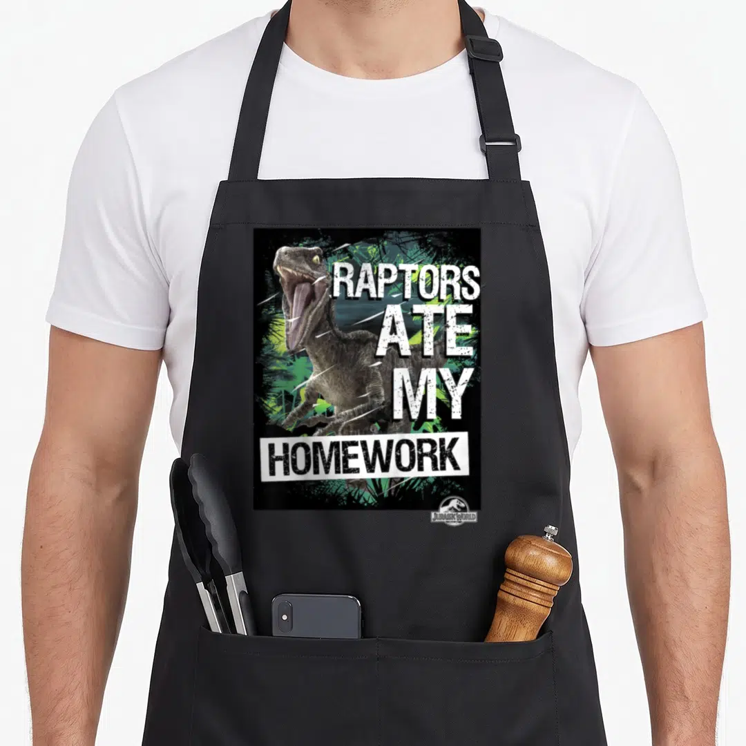 Jurassic ate homework apron - Realistic raptor next to stacked text reading Raptors Ate My Homework in white and black — shown on a black cotton canvas apron against a white background