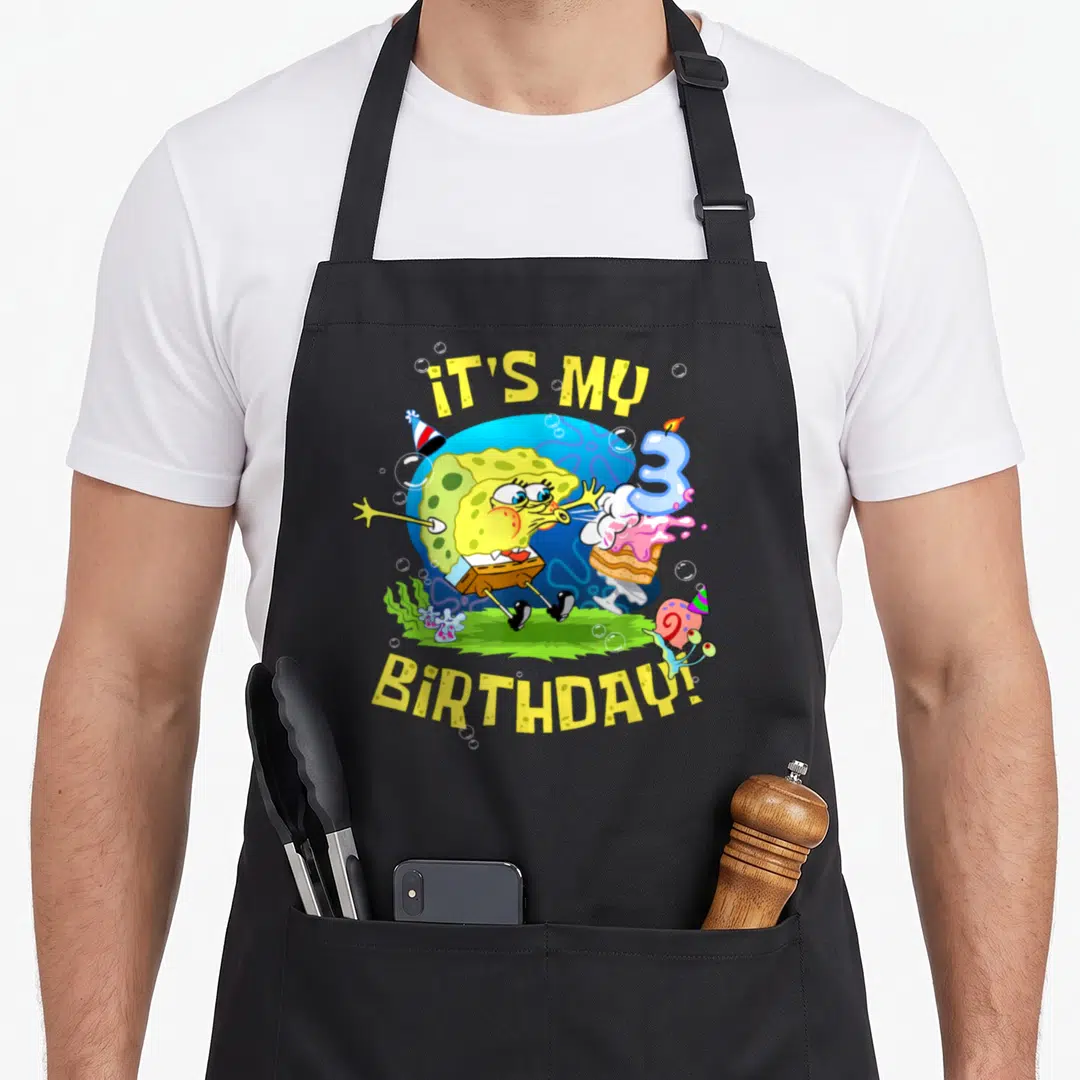 3rd cake apron - SpongeBob blowing out a number 3 candle with IT'S MY BIRTHDAY! text and Gary wearing a party hat — shown on a black cotton canvas apron against a white background