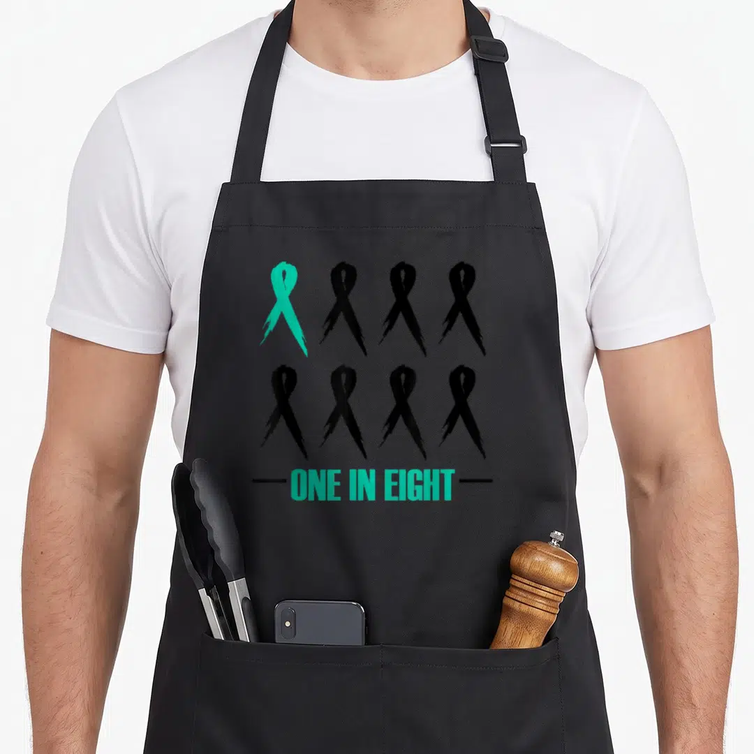 Eight ribbon apron - One teal and seven black awareness ribbons above ONE IN EIGHT text — shown on a black cotton canvas apron against a white background