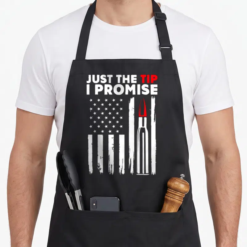 Tip bullet addict apron - Distressed US flag with a bullet replacing a stripe and text JUST THE TIP I PROMISE — shown on a black cotton canvas apron against a white background