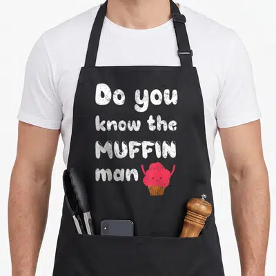 Food muffin man apron - Stacked white text Do you know the MUFFIN man next to a pink cartoon muffin with arms — shown on a black cotton canvas apron against a white background