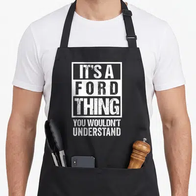 Ford family aprons - White distressed text IT'S A FORD THING YOU WOULDN'T UNDERSTAND stacked in five lines with framed — shown on a black cotton canvas apron against a white background