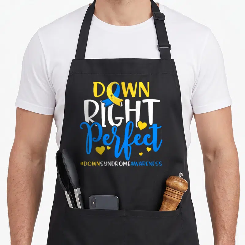 Syndrome chromosomes apron - Down Right Perfect text with smiling ribbon and yellow hearts — shown on a black cotton canvas apron against a white background