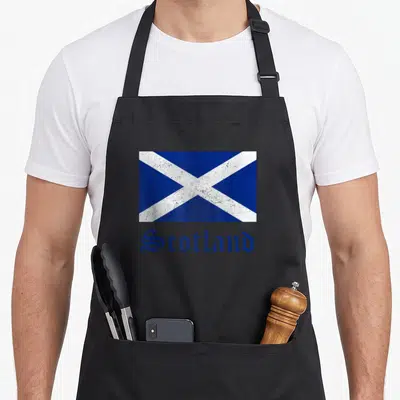 Scottish flag pride apron - Distressed blue white saltire flag with Scotland text printed on fabric — shown on a black cotton canvas apron against a white background