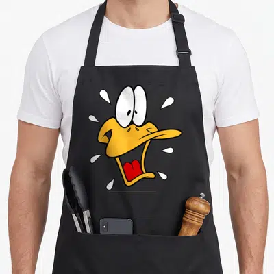 Surprised duck apron - Cartoon Daffy Duck head with white sweat drops and red tongue — shown on a black cotton canvas apron against a white background