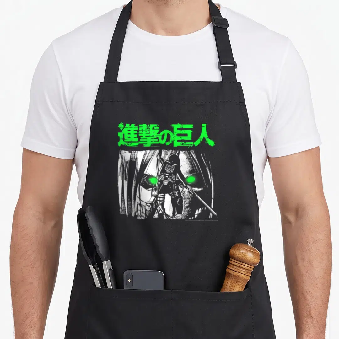 Eye anime apron - Green Japanese text above small character standing before large face with glowing green eyes — shown on a black cotton canvas apron against a white background