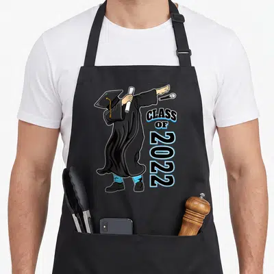 Senior school graduation apron - Cartoon graduate in black gown dabbing while holding a diploma next to vertical blue — shown on a black cotton canvas apron against a white background