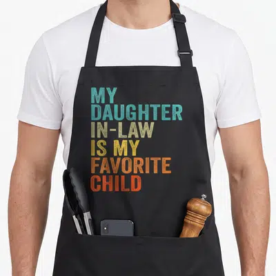 Funny law mom and daughter aprons - Stacked colorful text reading My Daughter In-Law Is My Favorite Child in teal beige — shown on a black cotton canvas apron against a white background