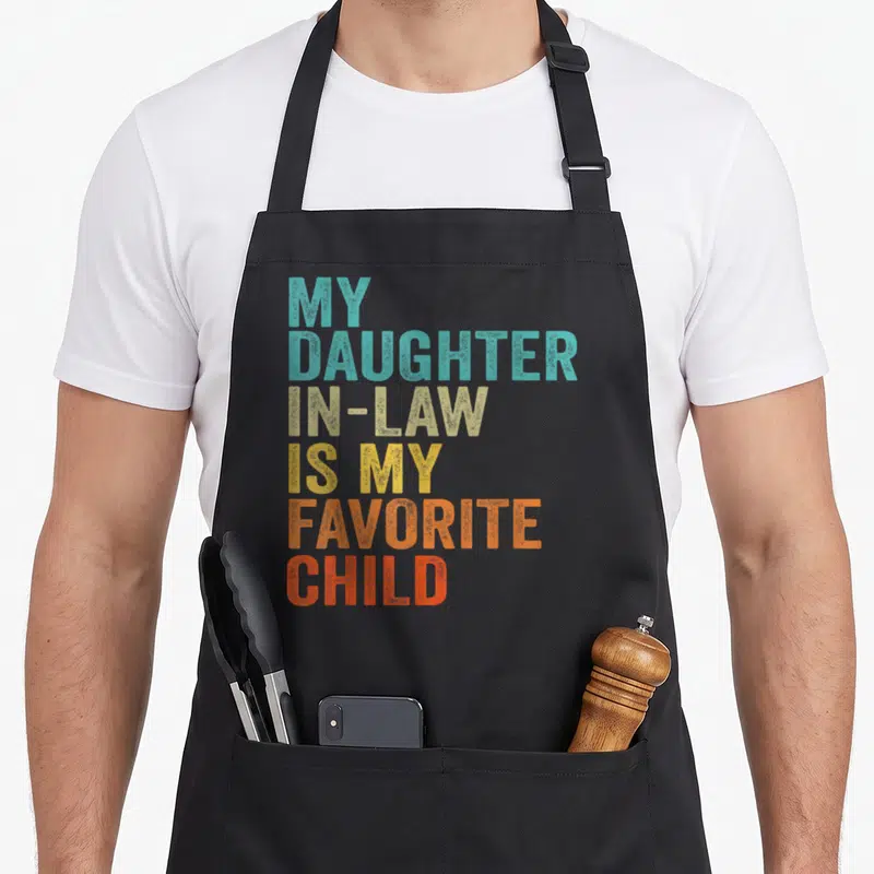 Funny law mom and daughter aprons - Stacked colorful text reading My Daughter In-Law Is My Favorite Child in teal beige — shown on a black cotton canvas apron against a white background