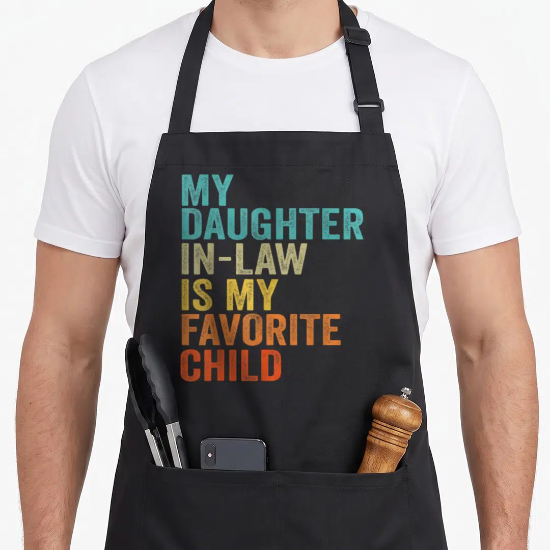 Funny law mom and daughter aprons - Stacked colorful text reading My Daughter In-Law Is My Favorite Child in teal beige — shown on a black cotton canvas apron against a white background