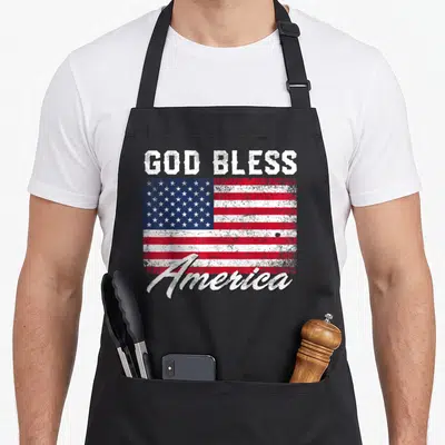God 4th of july apron - Distressed USA flag with God Bless America text in red white and blue — shown on a black cotton canvas apron against a white background