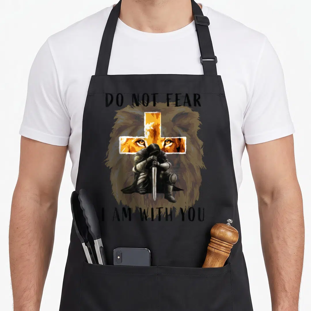 Faith bible verse apron - Lion head with orange cross, kneeling knight, DO NOT FEAR I AM WITH YOU text — shown on a black cotton canvas apron against a white background