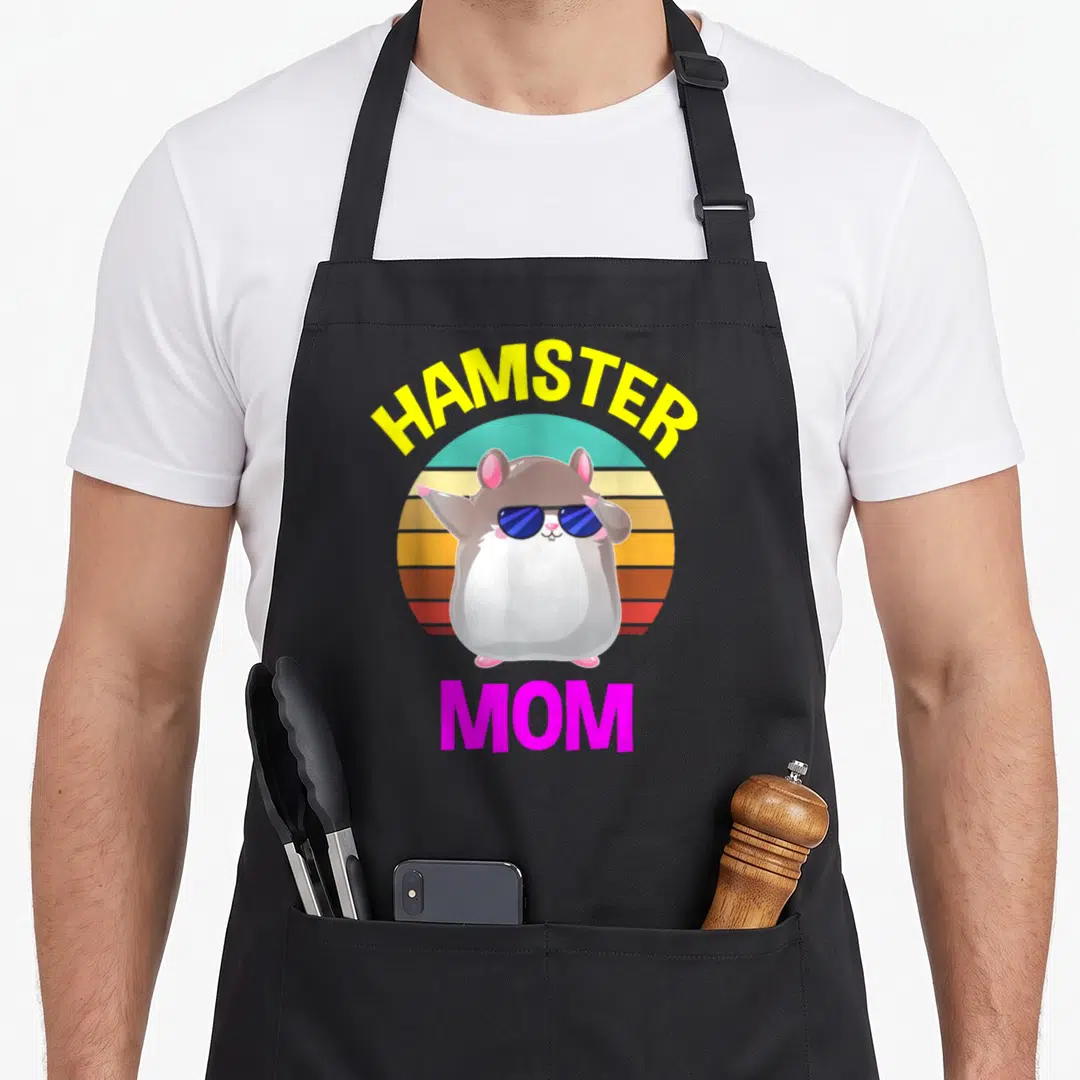 Costume mother's apron - Cartoon hamster with sunglasses on striped circle with HAMSTER MOM text — shown on a black cotton canvas apron against a white background