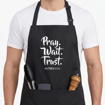 Wait christian apron - White stacked Pray Wait Trust typography with Matthew 21:22 reference — shown on a black cotton canvas apron against a white background