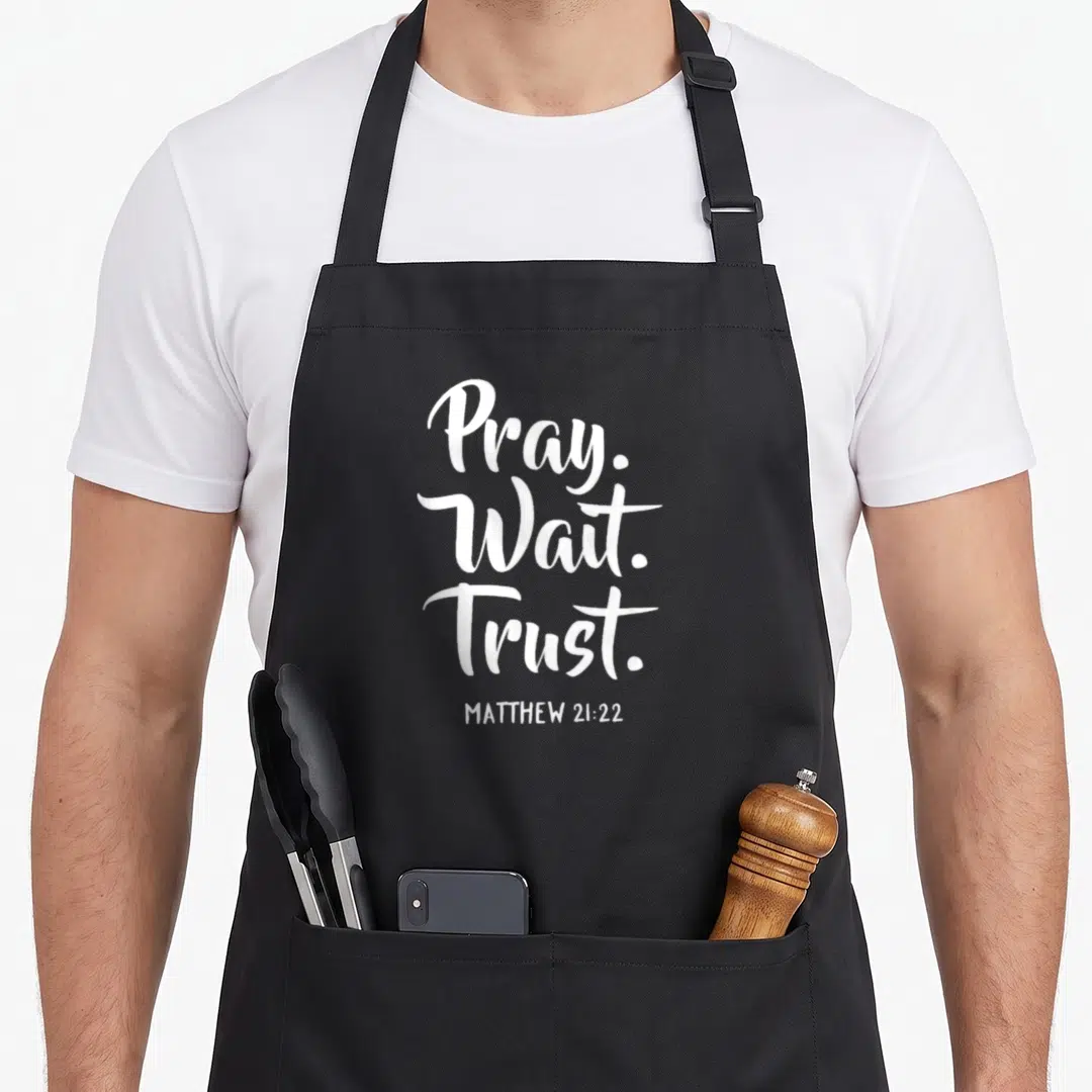 Wait christian apron - White stacked Pray Wait Trust typography with Matthew 21:22 reference — shown on a black cotton canvas apron against a white background