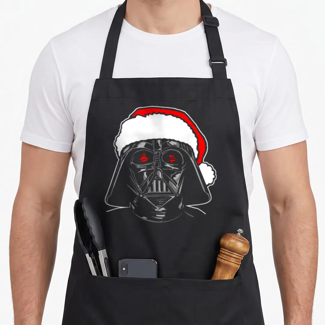 Christmas santa apron - Minimalist grey Darth Vader head wearing a red and white Santa hat with red eye accents — shown on a black cotton canvas apron against a white background