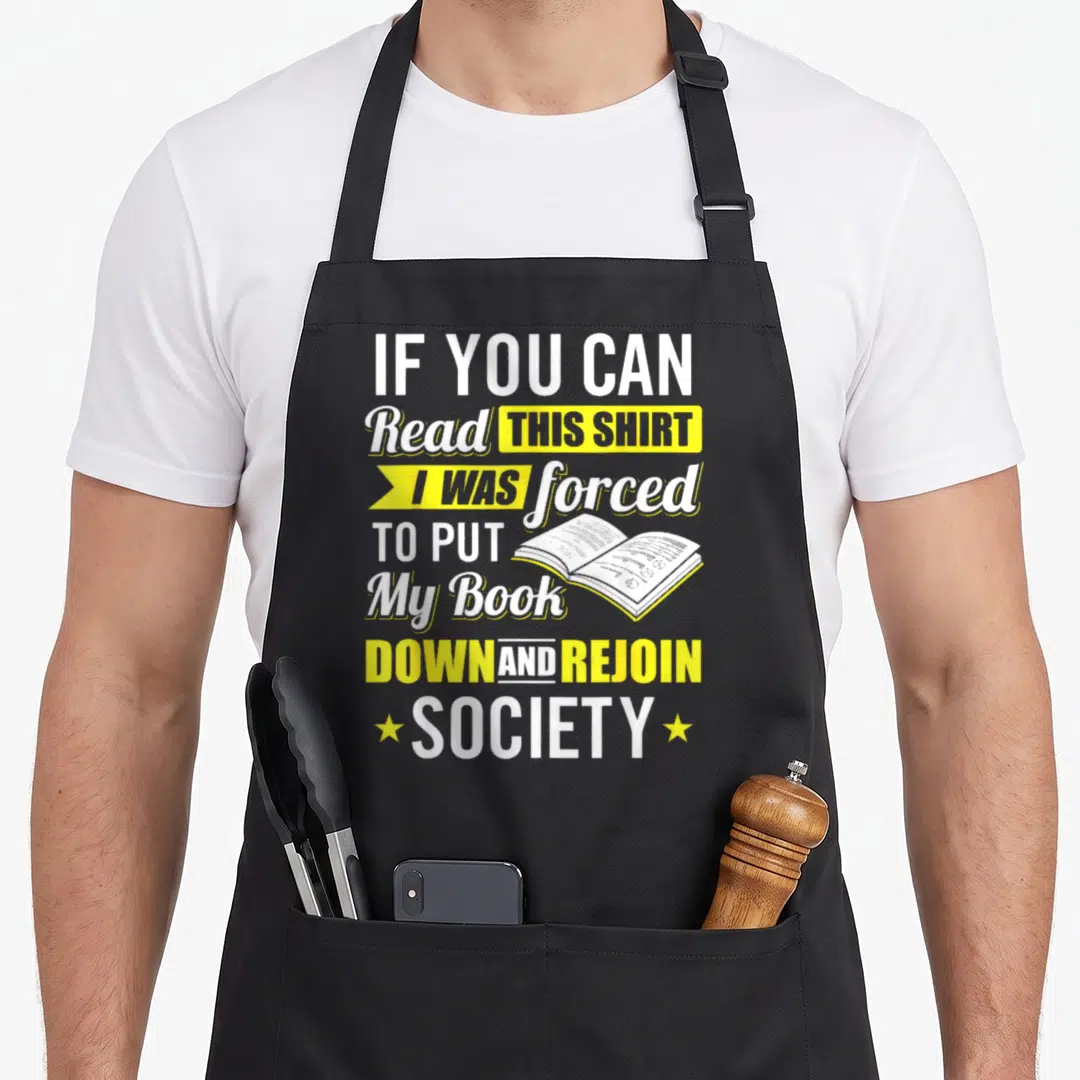 Forced funny book apron - Stacked white and yellow text with open book illustration and two stars — shown on a black cotton canvas apron against a white background
