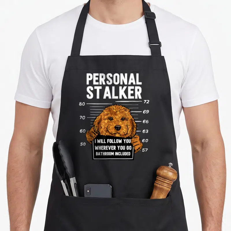 Cavapoo personal apron - Cartoon dog holding black sign in front of height chart with numbers — shown on a black cotton canvas apron against a white background