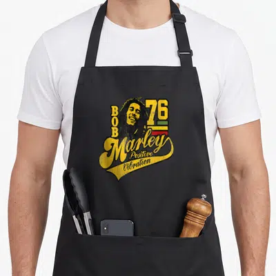 Bob soccer apron - Retro Bob Marley portrait with 76 and positive vibration script over colored stripes — shown on a black cotton canvas apron against a white background