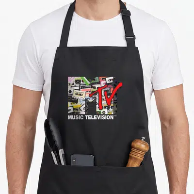Remix 80s apron - MTV logo with 3D M filled with cassette tapes and red TV text — shown on a black cotton canvas apron against a white background