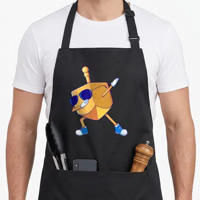 Dancing hanukkah apron - Cartoon orange dreidel wearing sunglasses, white gloves, and blue sneakers in a dynamic pose — shown on a black cotton canvas apron against a white background