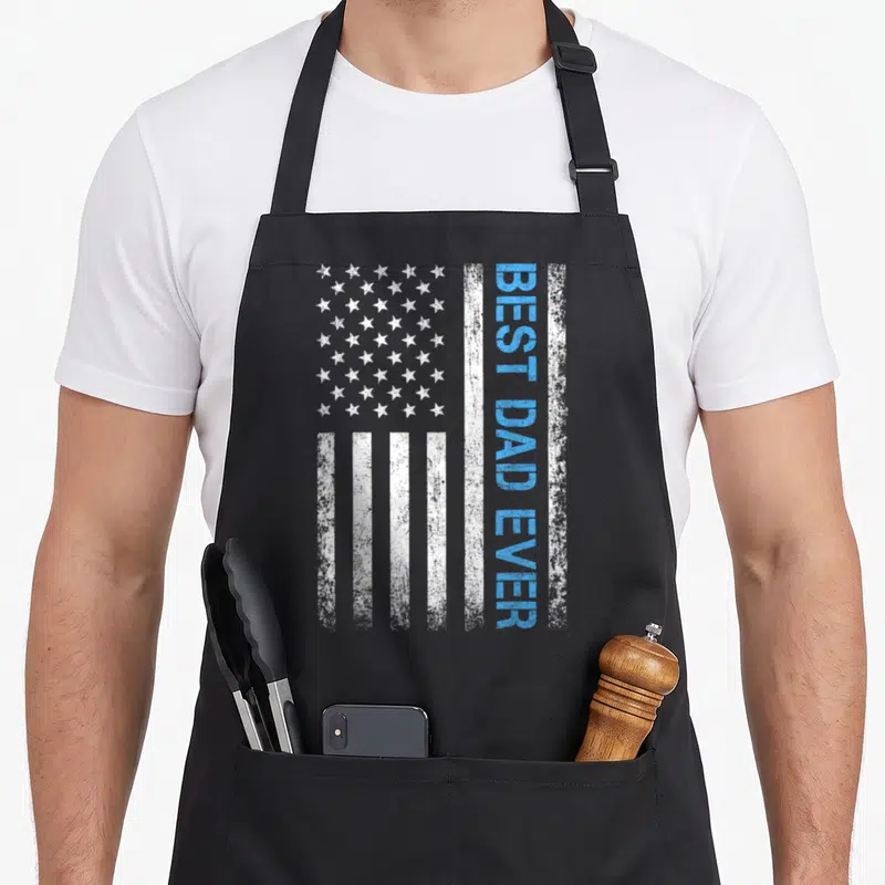 Vintage father american flag apron - Distressed USA flag with vertical blue BEST DAD EVER text on white stripe — shown on a black cotton canvas apron against a white background