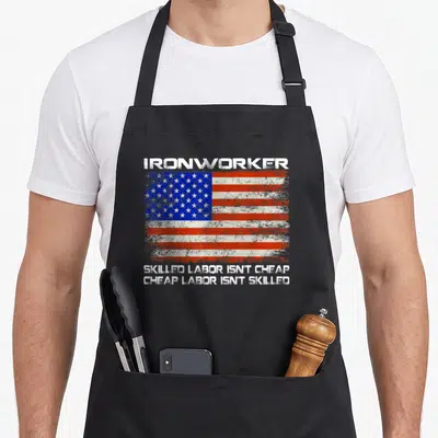 Ironworker american flag apron - Distressed USA flag with ironworker text and skilled labor quote on black fabric — shown on a black cotton canvas apron against a white background