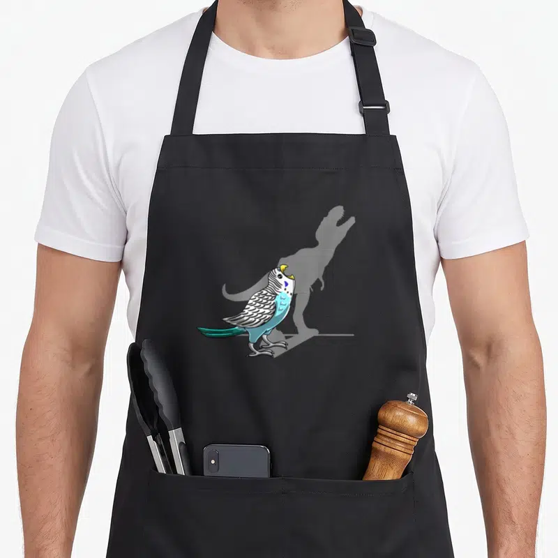 Rex bird apron - Blue and white budgie with open beak casting a grey T-Rex shadow — shown on a black cotton canvas apron against a white background