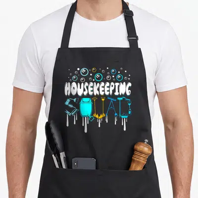 Squad housekeeper apron - HOUSEKEEPING SQUAD text formed by cyan and orange cleaning tools with white drips and bubbles — shown on a black cotton canvas apron against a white background