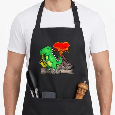 Music dinosaur apron - Green cartoon dinosaur playing yellow saxophone in front of erupting red volcano — shown on a black cotton canvas apron against a white background