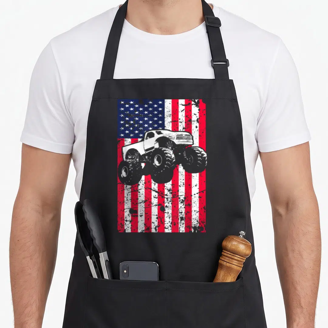 Monster racing apron - Grey monster truck centered on distressed red white blue American flag background — shown on a black cotton canvas apron against a white background