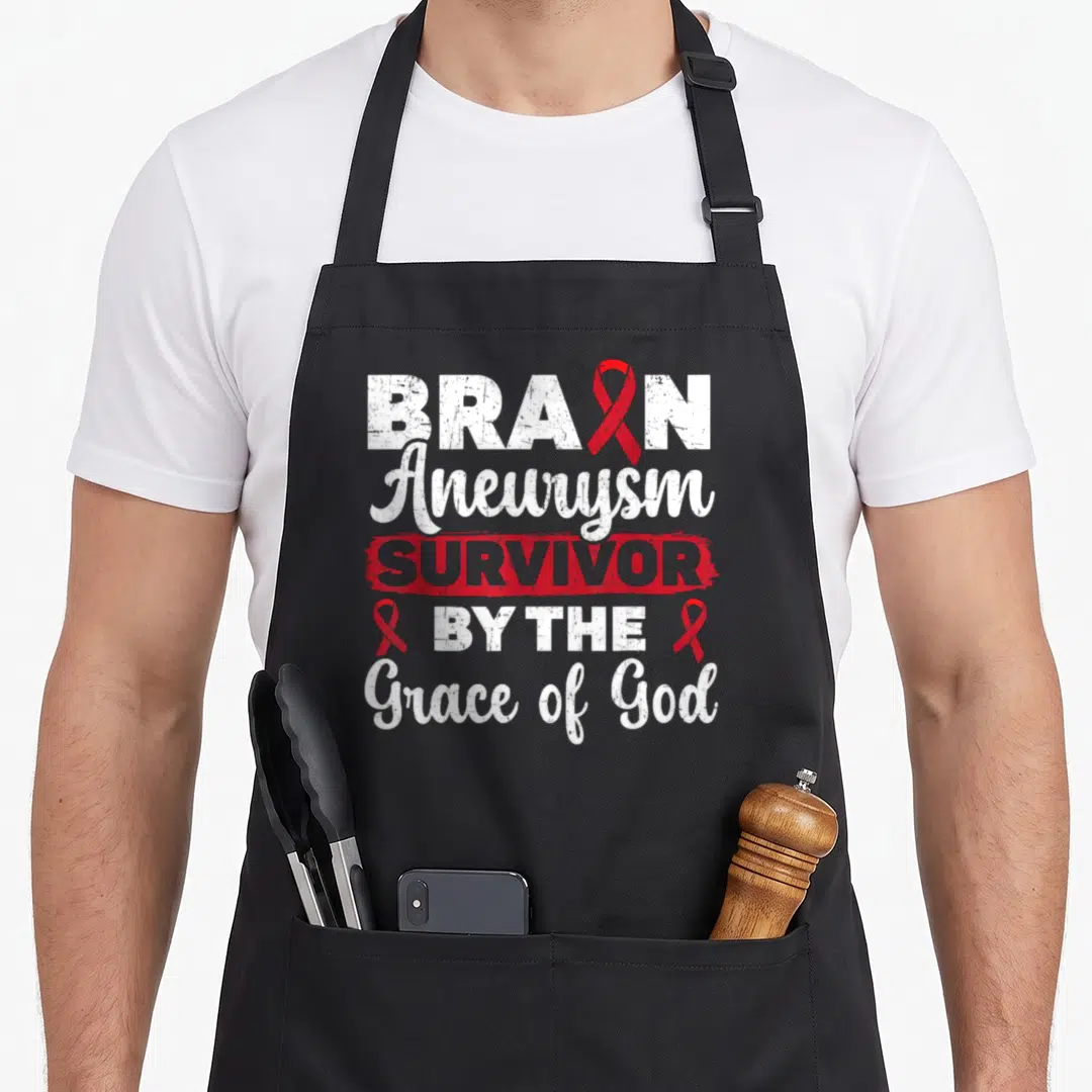 Survivor aneurysm awareness apron - Stacked text reading BRAIN Aneurysm SURVIVOR BY THE Grace of God with red ribbons — shown on a black cotton canvas apron against a white background