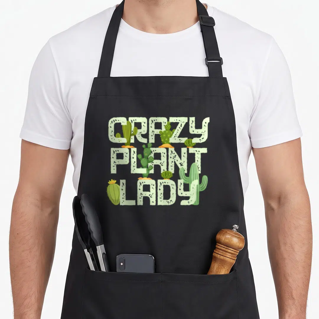 Vintage gardening plant lady apron - Stacked CRAZY PLANT LADY text with overlapping green cacti illustrations — shown on a black cotton canvas apron against a white background