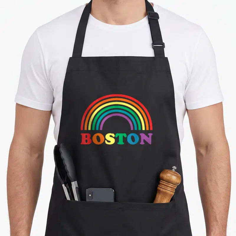 Parade gay pride apron - Rainbow arch above BOSTON text with letters in red orange yellow green blue and purple — shown on a black cotton canvas apron against a white background