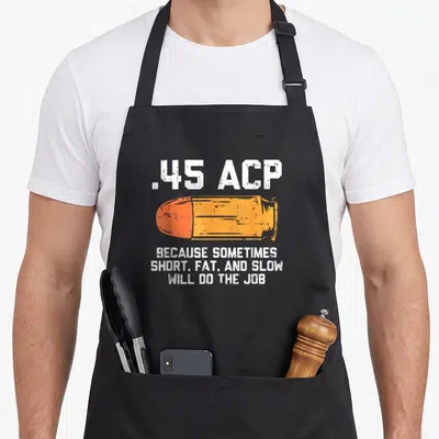 Sometime fat man in apron - Orange bullet graphic with white distressed text reading .45 ACP Because Sometimes Short — shown on a black cotton canvas apron against a white background