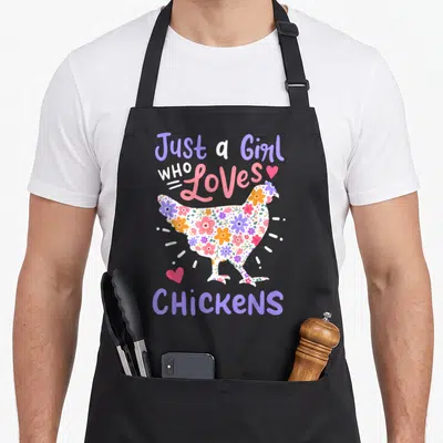 Chicken hen apron - Floral patterned chicken silhouette surrounded by purple and pink text reading Just a Girl Who — shown on a black cotton canvas apron against a white background