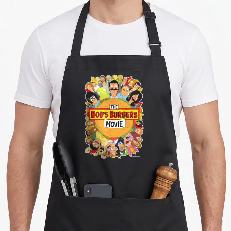 Poster bobs burger apron - Hamburger with THE BOB'S BURGERS MOVIE text surrounded by cartoon characters in orange — shown on a black cotton canvas apron against a white background