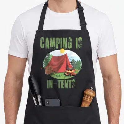 Tent happy camper apron - Red tent campfire cartoon scene with Camping Is In-Tents text — shown on a black cotton canvas apron against a white background