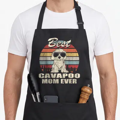 Vintage cavapoo dog apron - Retro dog with sunglasses in front of striped sunset with text Best Cavapoo Mom Ever — shown on a black cotton canvas apron against a white background